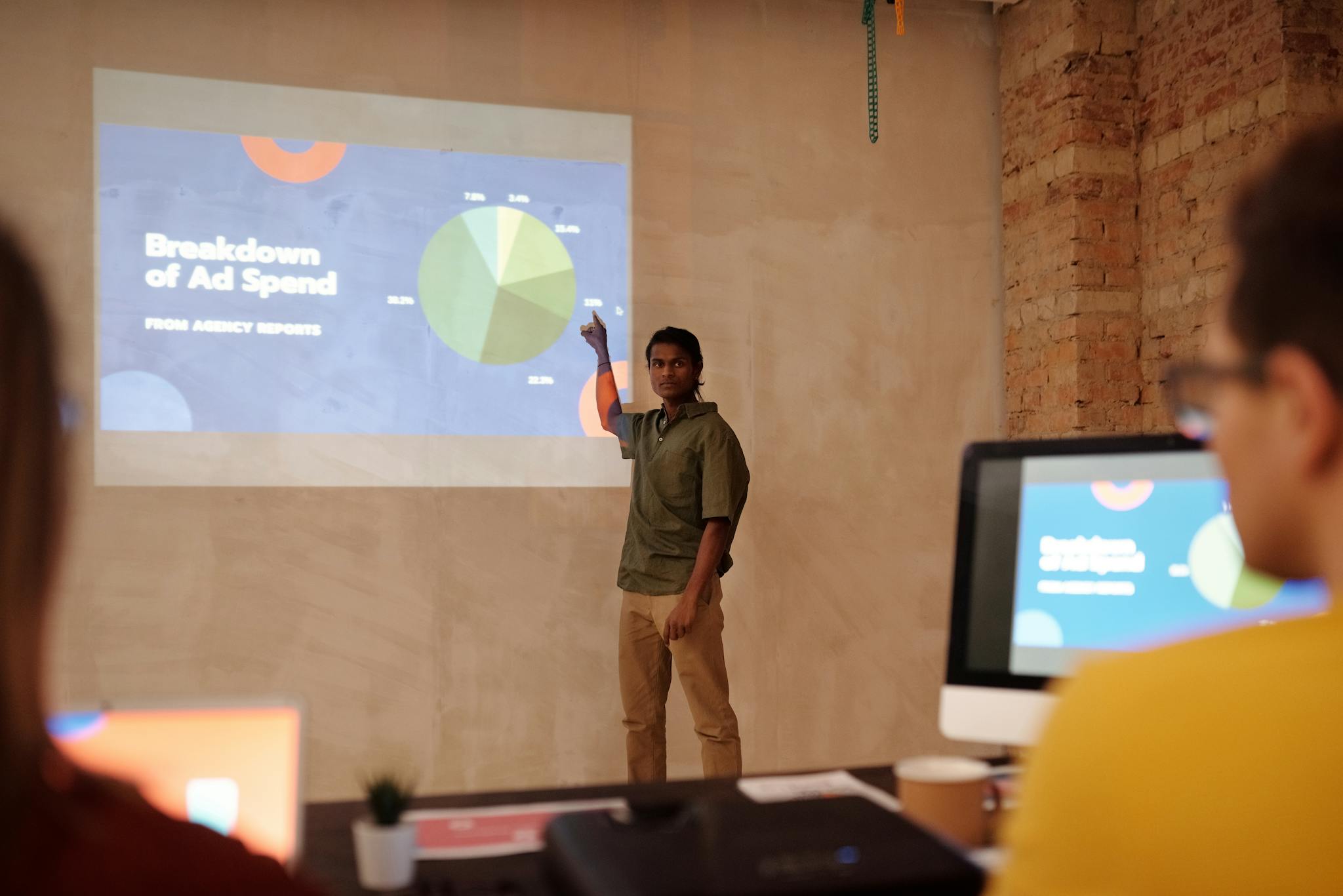 About 3 Young man delivering a business presentation on ad spend with charts and graphs in a modern office setting.